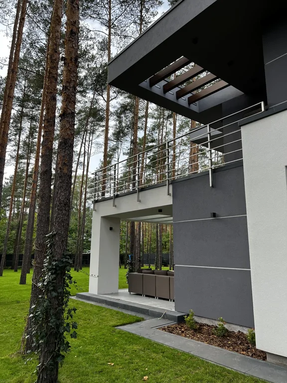 Detal tarasu i balkonu: pergola w okapie, stalowa balustrada, strefa wypoczynku i rabata przy elewacji