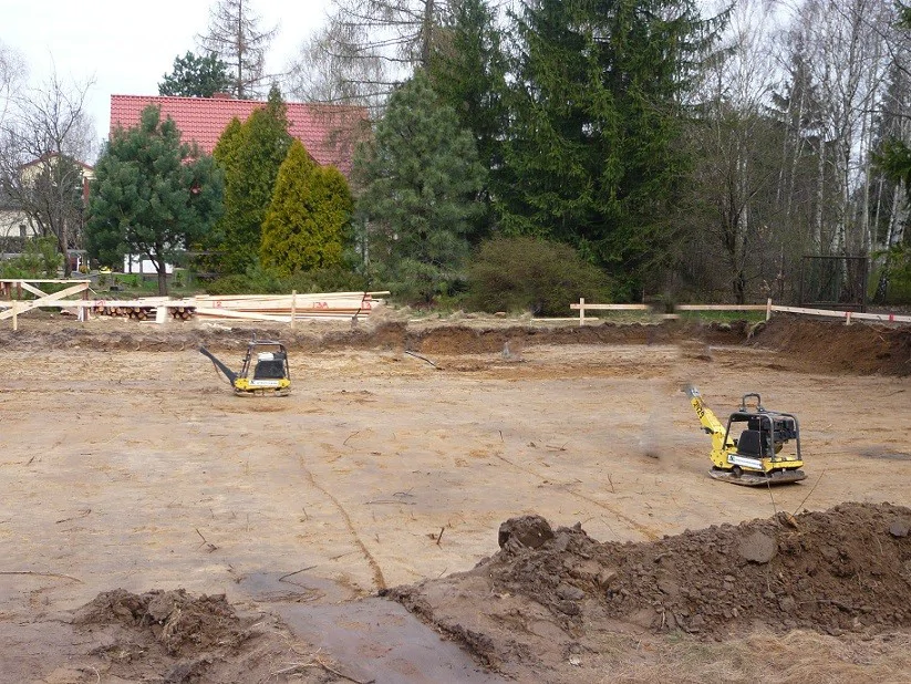 Przygotowanie podłoża pod płytę fundamentową – wyrównany piasek i zagęszczarki na działce