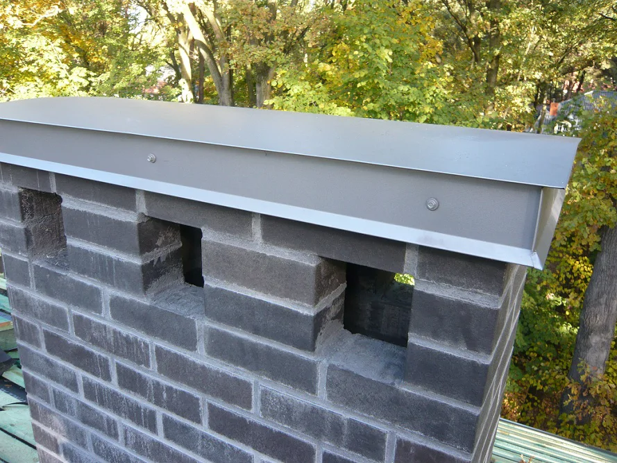 Komin murowany z nową czapą/obróbką z blachy; detal wykończenia na dachu.