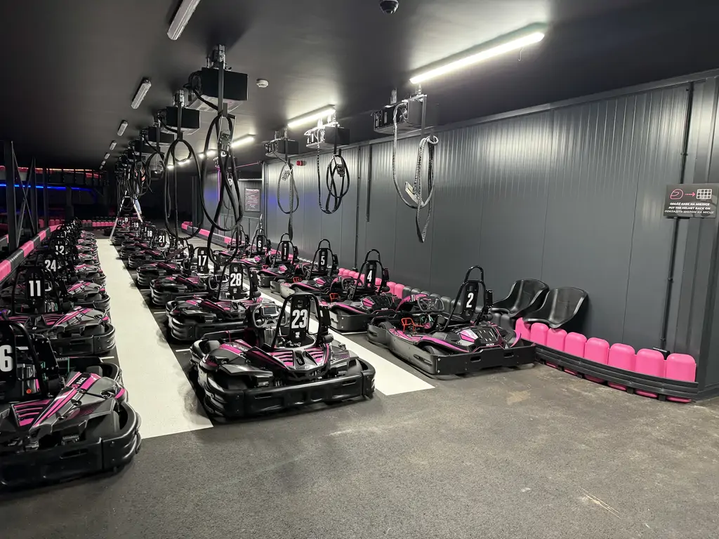Strefa postojowa gokartów elektrycznych z numerowanymi pojazdami i systemem podwieszanego ładowania.