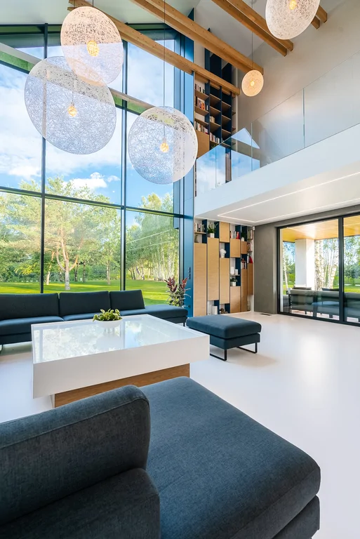 Dwukondygnacyjny salon z dużymi lampami wiszącymi i przeszkloną antresolą.