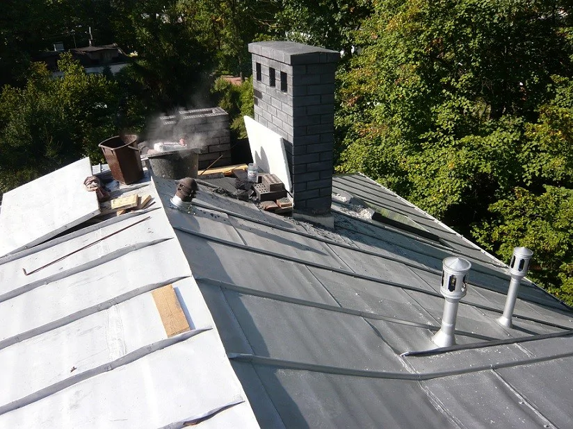 Prace na dachu z blachy: widok połaci z kominem i wywiewkami wentylacyjnymi.