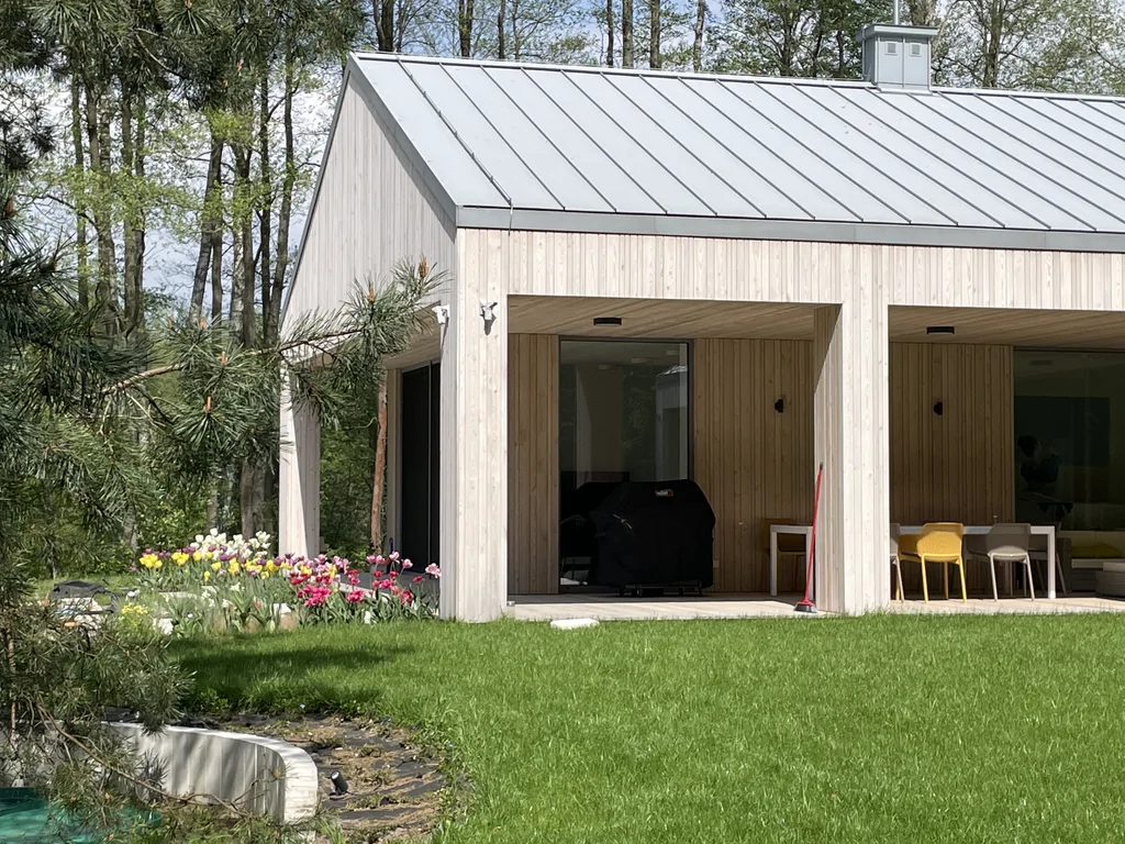 Widok dziedzińca domu z dużymi przeszkleniami i zielonym trawnikiem