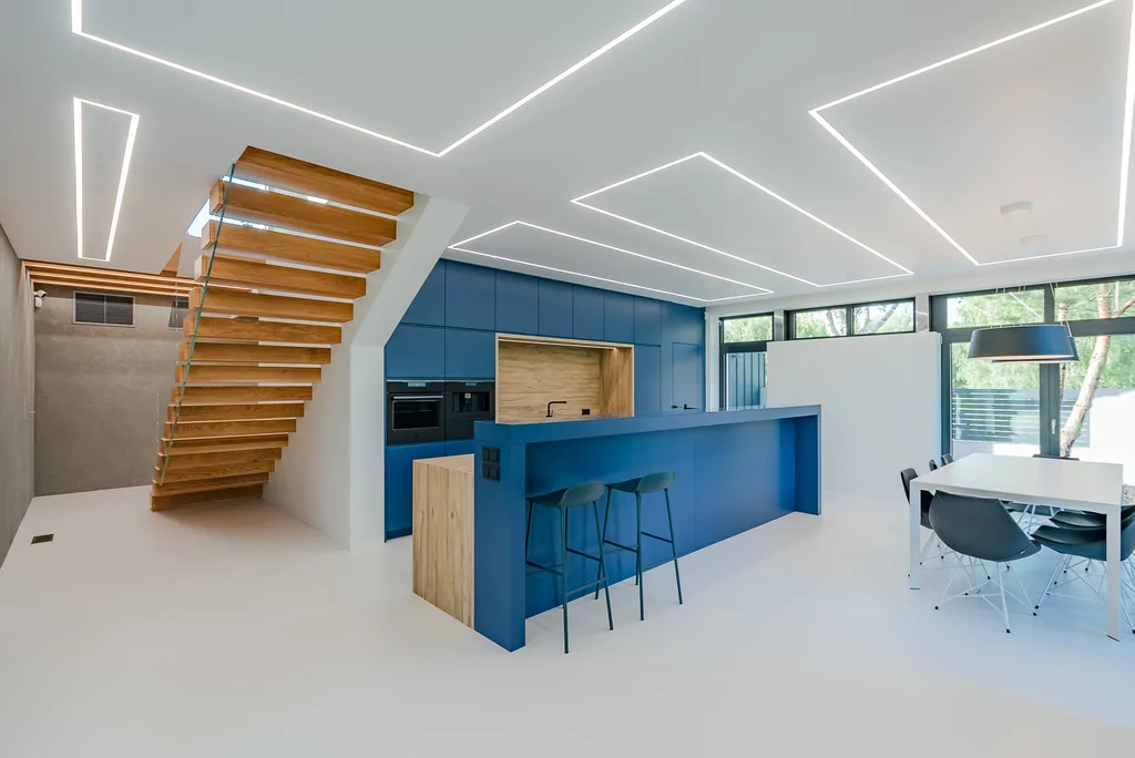 Otwarta strefa dzienna z kuchnią, granatową wyspą i schodami wspornikowymi.