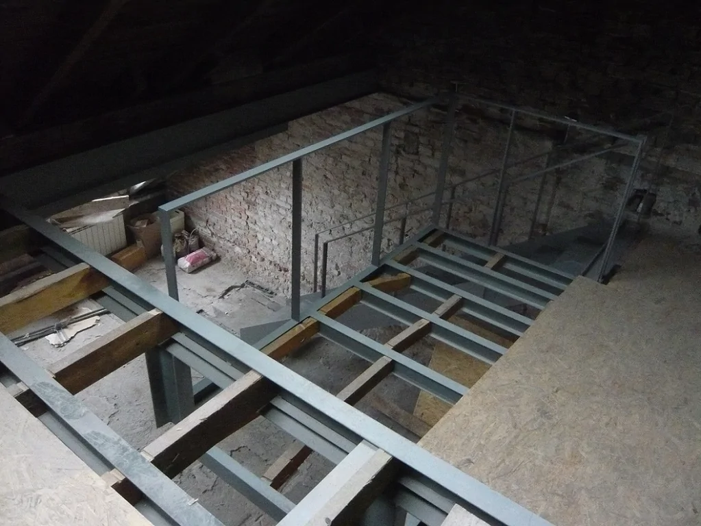 Widok z góry na konstrukcję antresoli pod skosem dachu, stalowe belki i tymczasowa płyta OSB