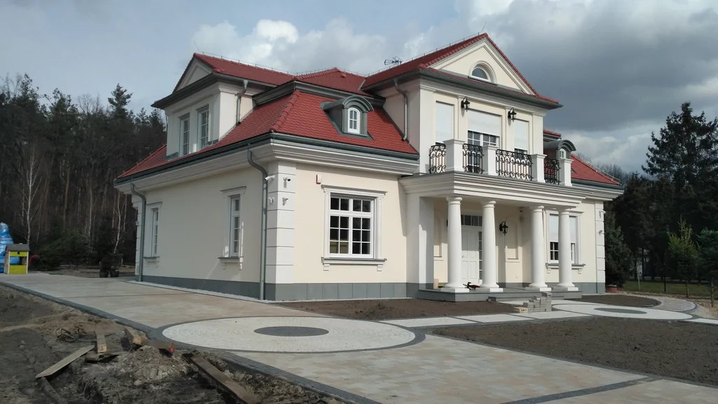 Budowa domu jednorodzinnego, styl dworkowy, dachówka z karpiówki, biała elewacja, bonie, lukarny, kominy, biała stolarka okienna, kolumny, kostka 