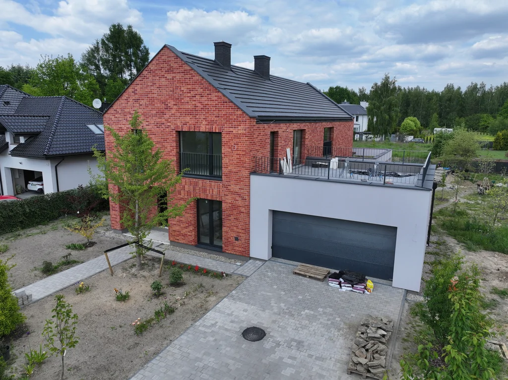 Widok frontowy z drona na dom z ceglaną elewacją, garażem i uporządkowaną strefą wejściową