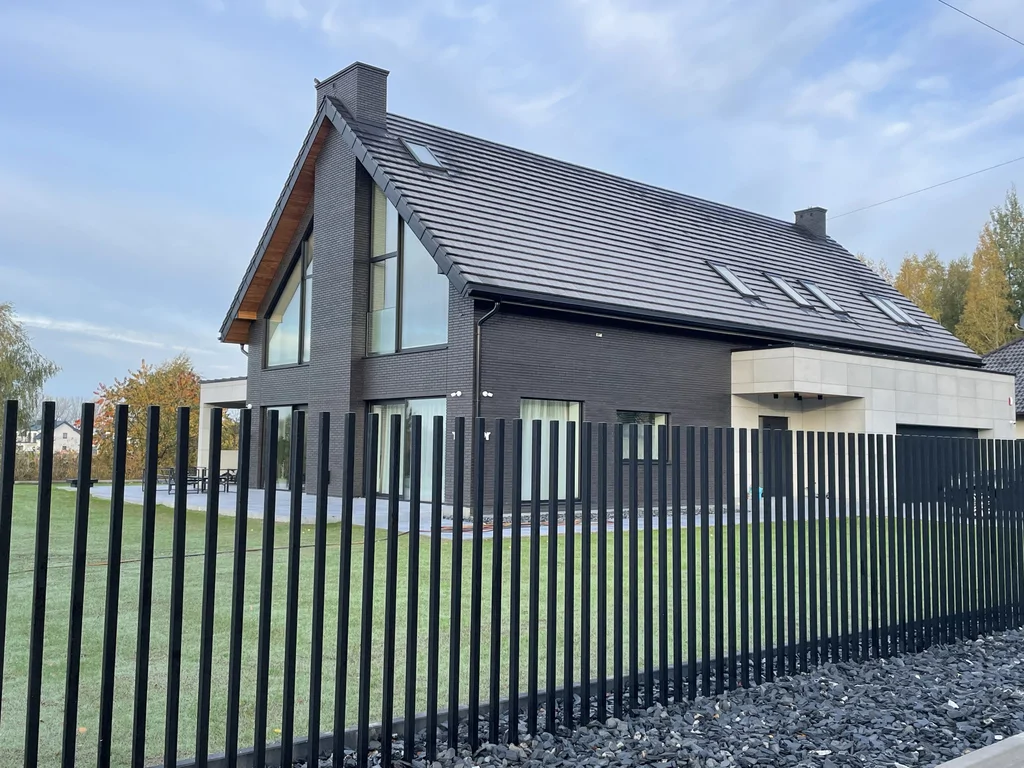 Dom jednorodzinny w Ruścu – elewacja z cegły klinkierowej, widok zza stalowego ogrodzenia