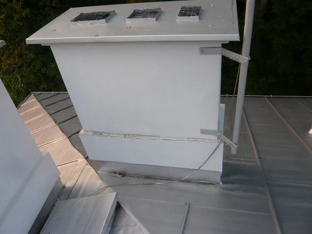 Detal na dachu: obudowa/wywietrznik instalacyjny na pokryciu z blachy z mocowaniami.