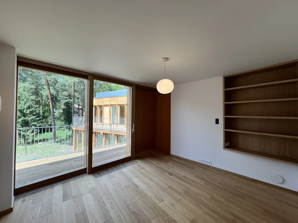 Pokój z dużym przeszkleniem, drewnianą podłogą i zabudową regałową przy wyjściu na balkon