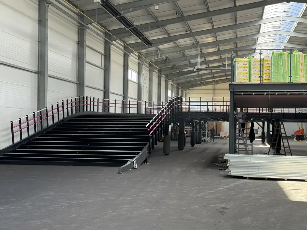 Wnętrze hali gokartowej podczas prac wykończeniowych, z czarną rampą, antresolą i konstrukcją stalową.