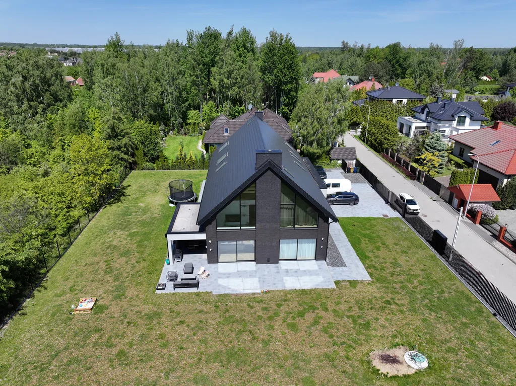 Ujęcie z drona: elewacja szczytowa domu w Ruścu, duże przeszklenie i taras od strony ogrodu.