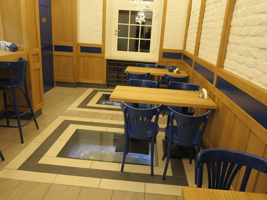 zdjęcie piekarni wewnątrz, stoliki krzesła, posadzka z podświetlanymi otworami, na ścianach kamień i drewno 