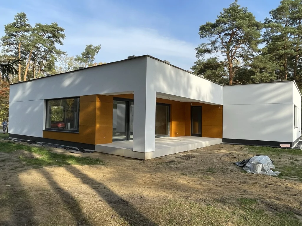 Taras i elewacja nowoczesnego domu parterowego z dużymi przeszkleniami i białą geometryczną bryłą