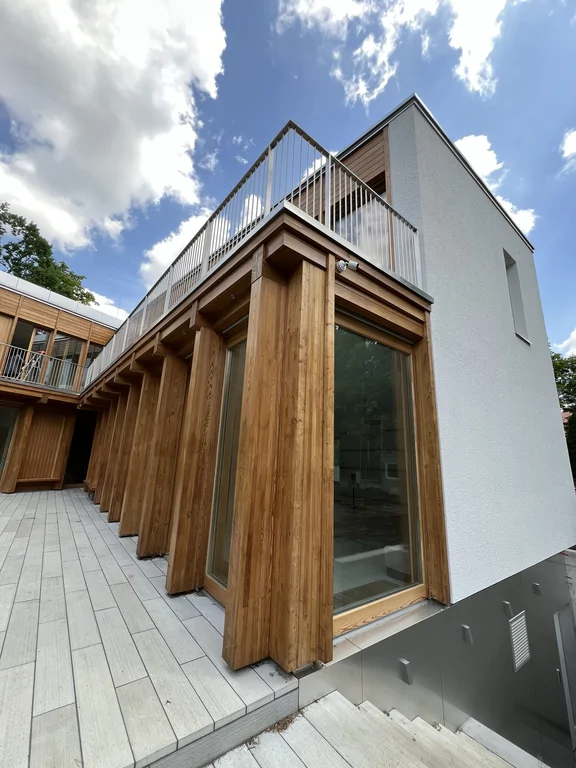 Narożna elewacja budynku z dużymi przeszkleniami, drewnianymi słupami i schodami zewnętrznymi