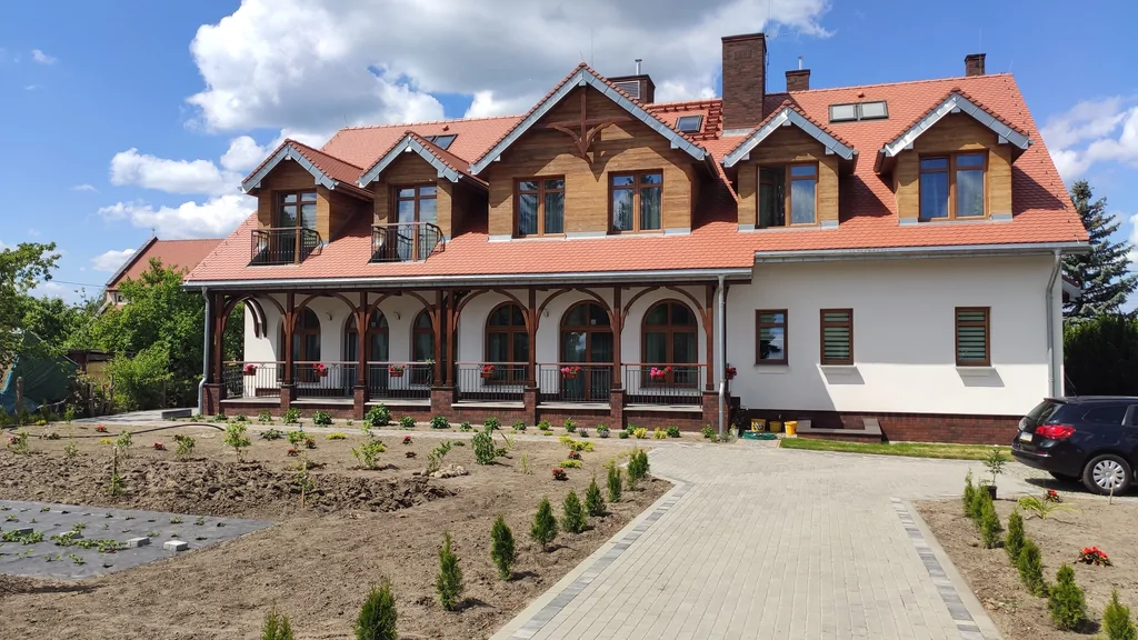 Wejście główne do domu zakonnego w Ostródzie, widok pod kątem z alejką, schodami i drewnianym zadaszeniem