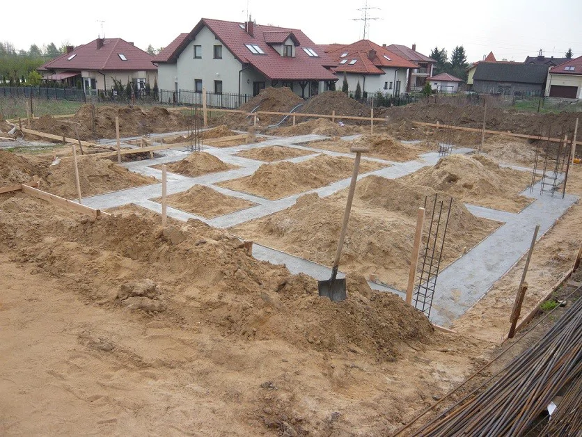 Wylane ławy fundamentowe w wykopie, widoczne pręty zbrojeniowe i prace ziemne