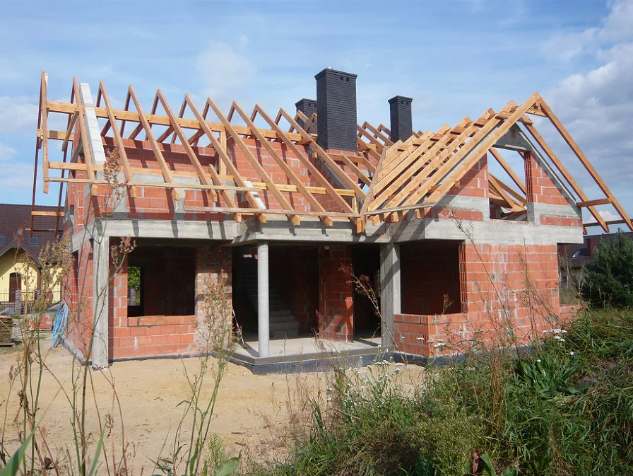 Więźba dachowa w trakcie montażu – widok na rozbudowaną bryłę i otwory okienne