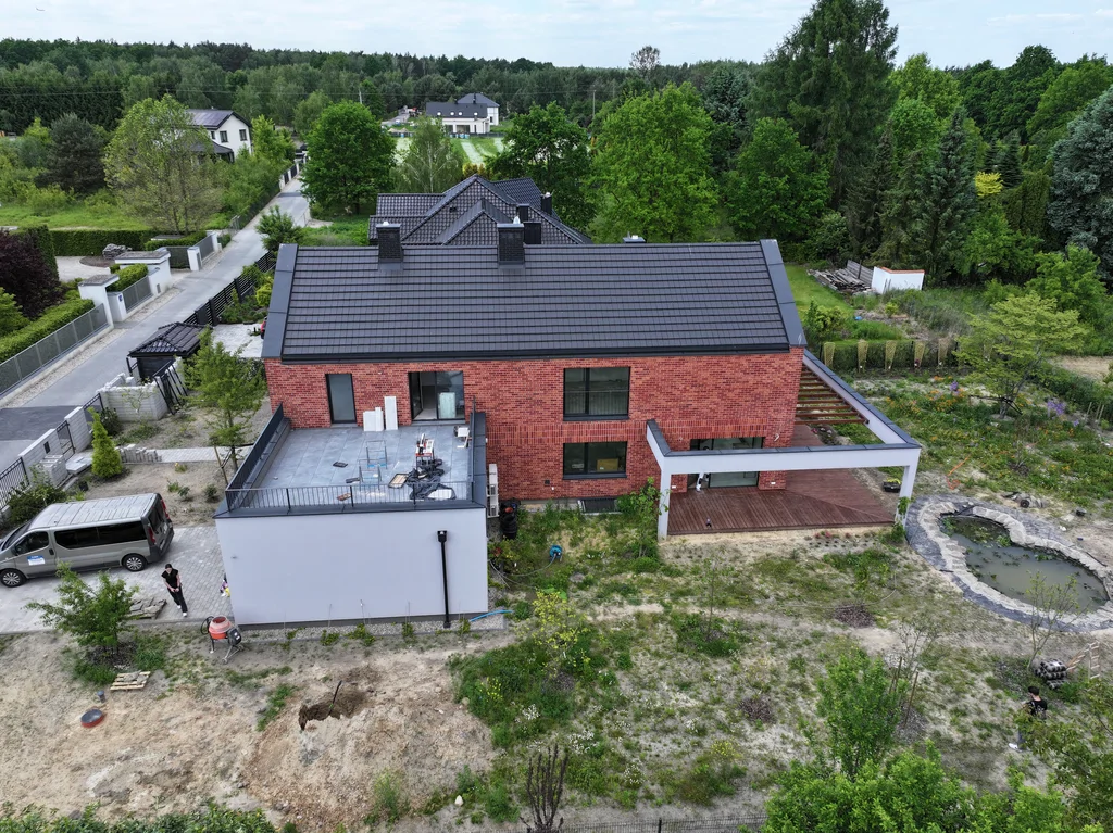 Panoramiczny widok z drona na tył domu z dachem dwuspadowym, tarasem dachowym nad garażem i ogrodem