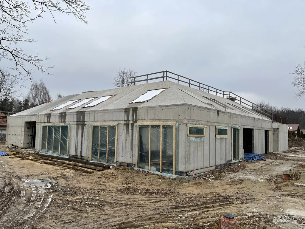 Widok narożnika: ściany z betonu architektonicznego i żelbetowy dach po skosie z otworami doświetlającymi