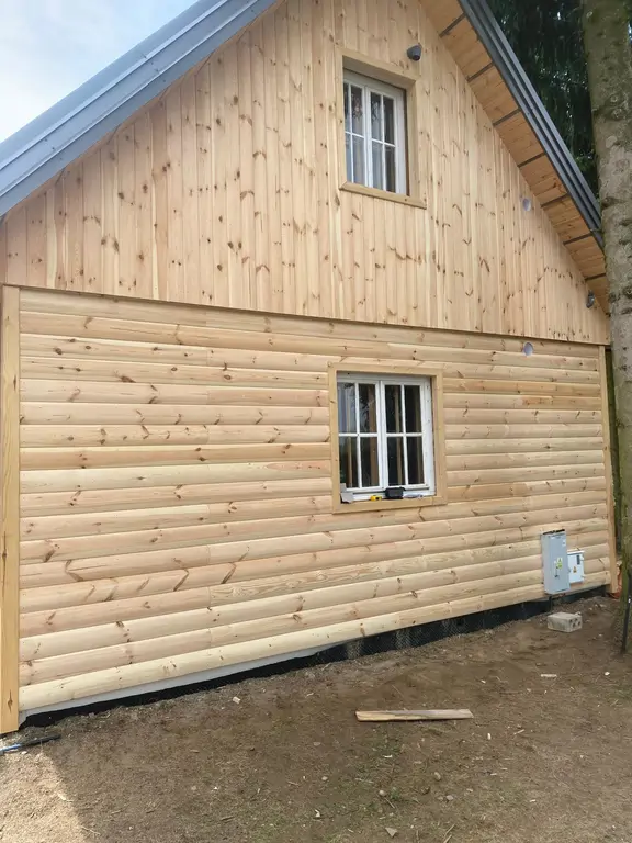 Domek drewniany z odnowiona elewacja i białą stolarka okienna 