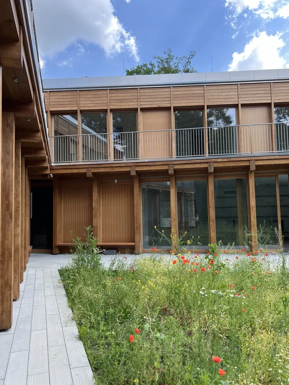 Frontowy widok na wewnętrzny dziedziniec z łąką kwietną i drewnianą elewacją budynku