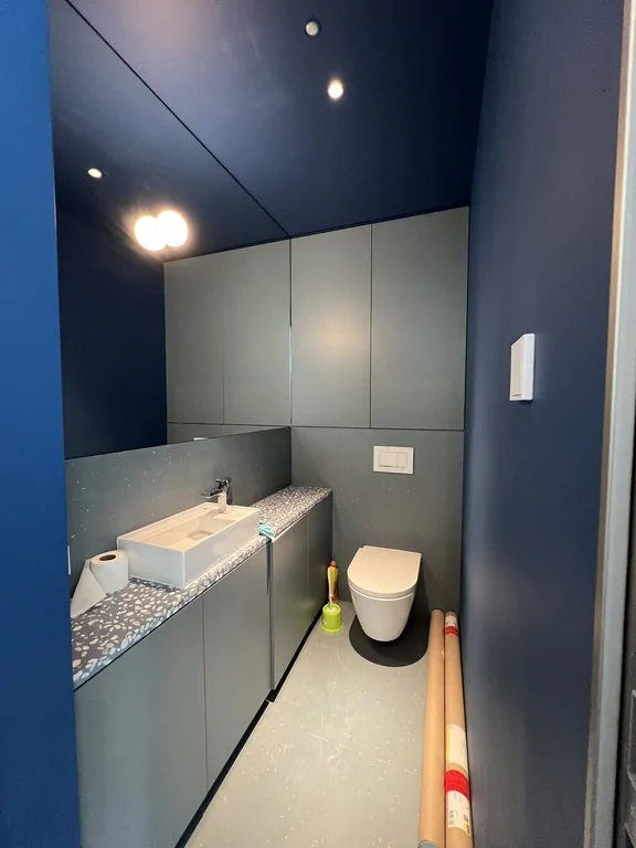 Mała łazienka w granatowej kolorystyce z umywalką, zabudową i podwieszaną toaletą