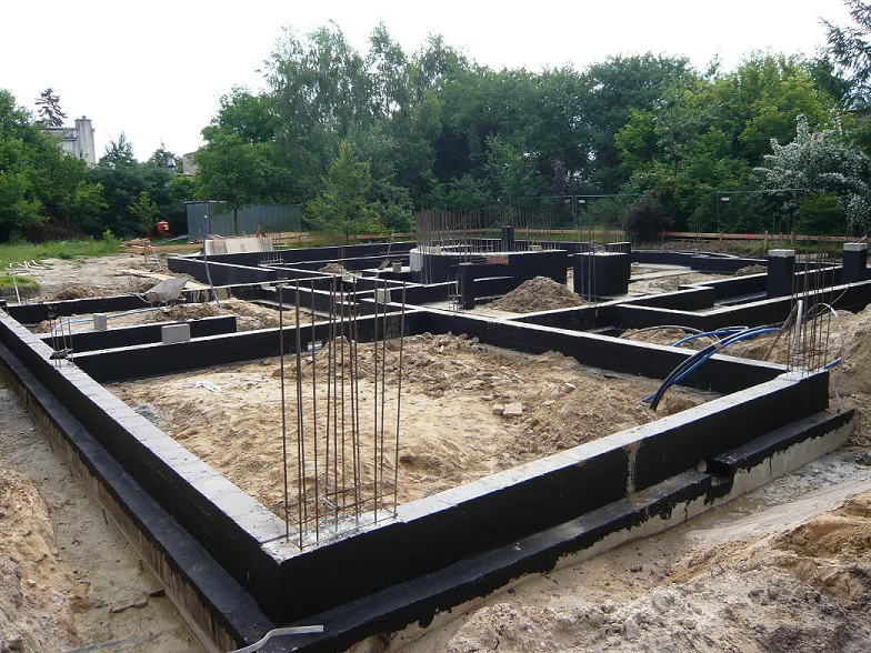 ściany fundamentowe z hydroizolacją bitumiczną i wystającym zbrojeniem na budowie