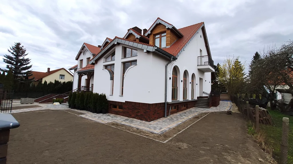 Dom zakonny w Ostródzie, widok na narożnik budynku z arkadami, czerwonym dachem i chodnikiem z kostki brukowej