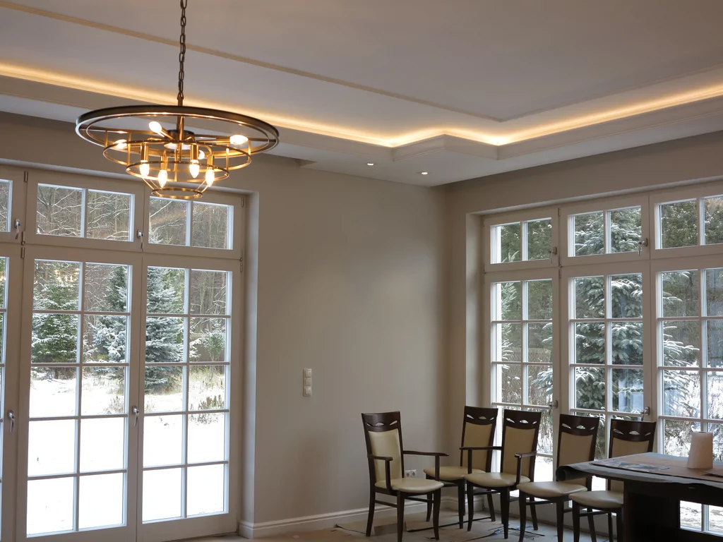 widok na białą łazienkę, w łazience białe płytki i meble, duża białą zdobiona wanna, duże lustro i obraz 