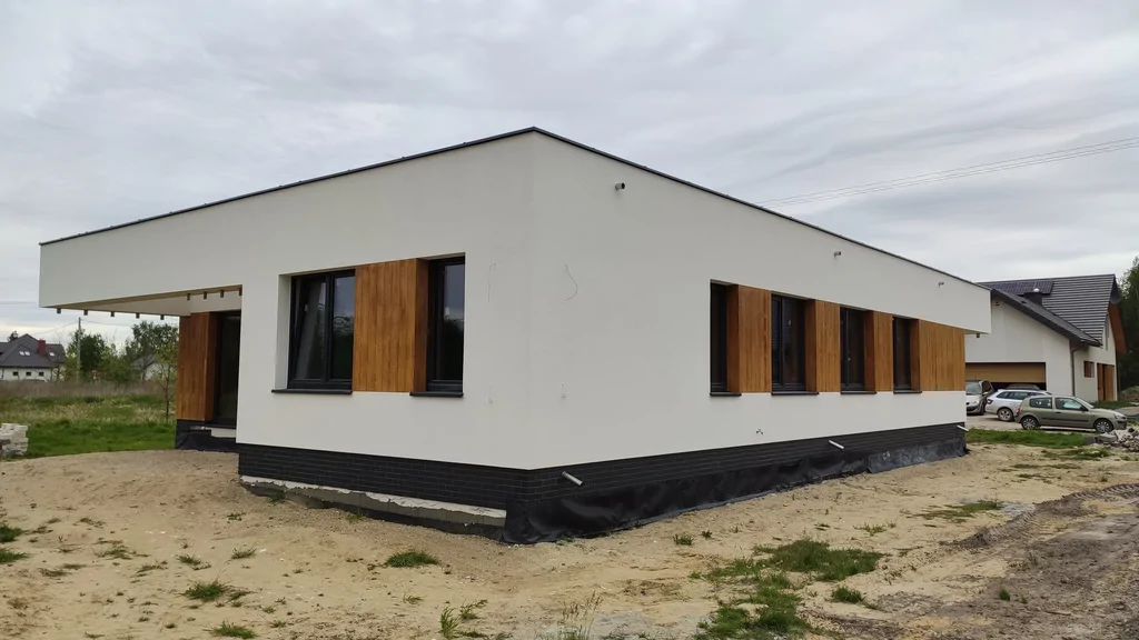 Budynek w stanie deweloperskim, ciemna stolarka okienna, jasna elewacja i elementy okładzina imitująca drewno 