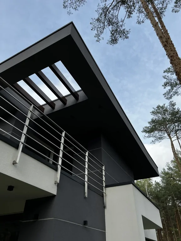 Widok z dołu na duży okap i pergolę w dachu; stalowa balustrada balkonu na tle nieba