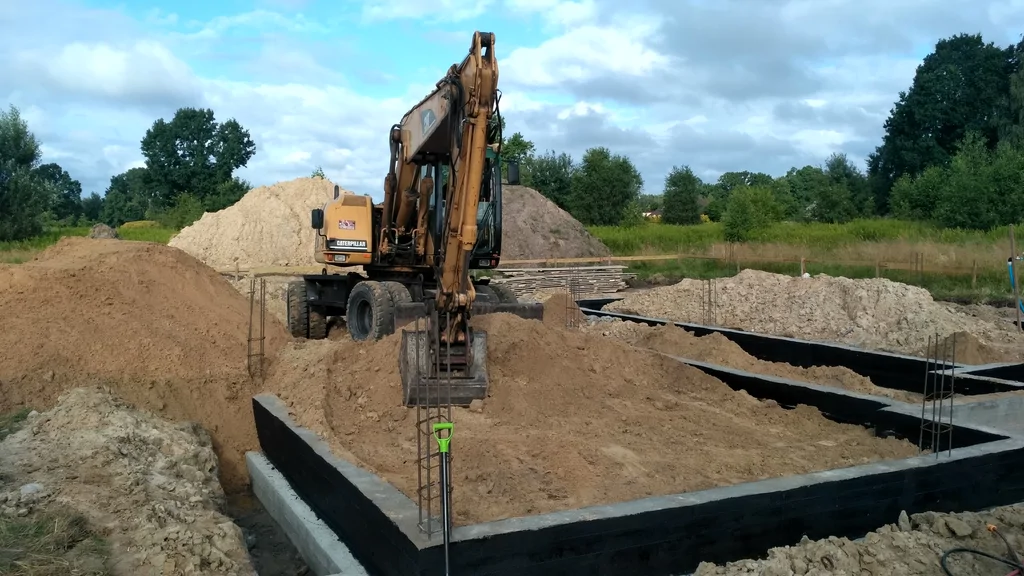 Wykonane fundamenty, prace zasypowe, w tle koparka 