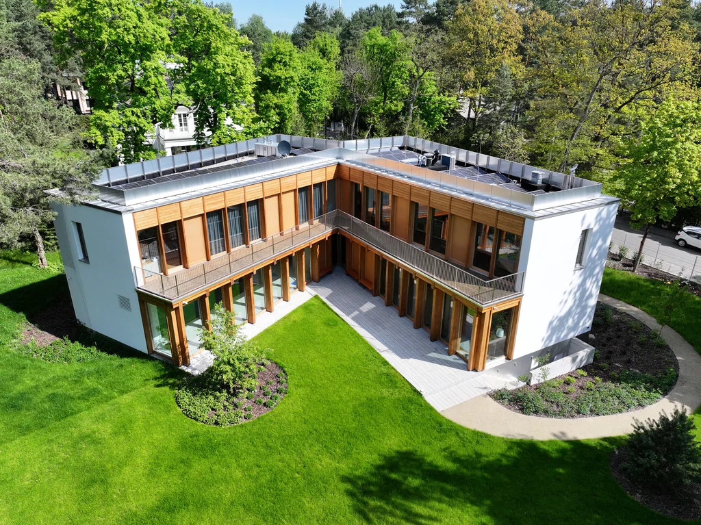 Widok z drona na nowoczesny dom z wewnętrznym patio, drewnianą elewacją i dużym tarasem otaczającym trawnik