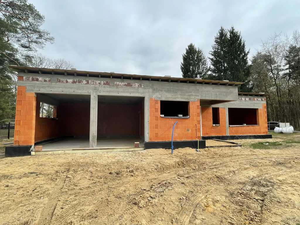 Bryła domu jednorodzinnego w stanie surowym z widoczną strefą garażową i dużymi otworami okiennymi