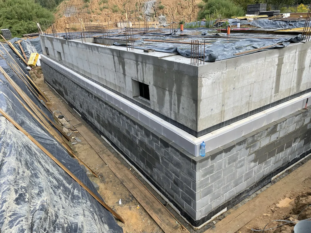 Ściany piwnicy z wykonanym ociepleniem i izolacją przygotowane do dalszych prac ziemnych oraz zasypania