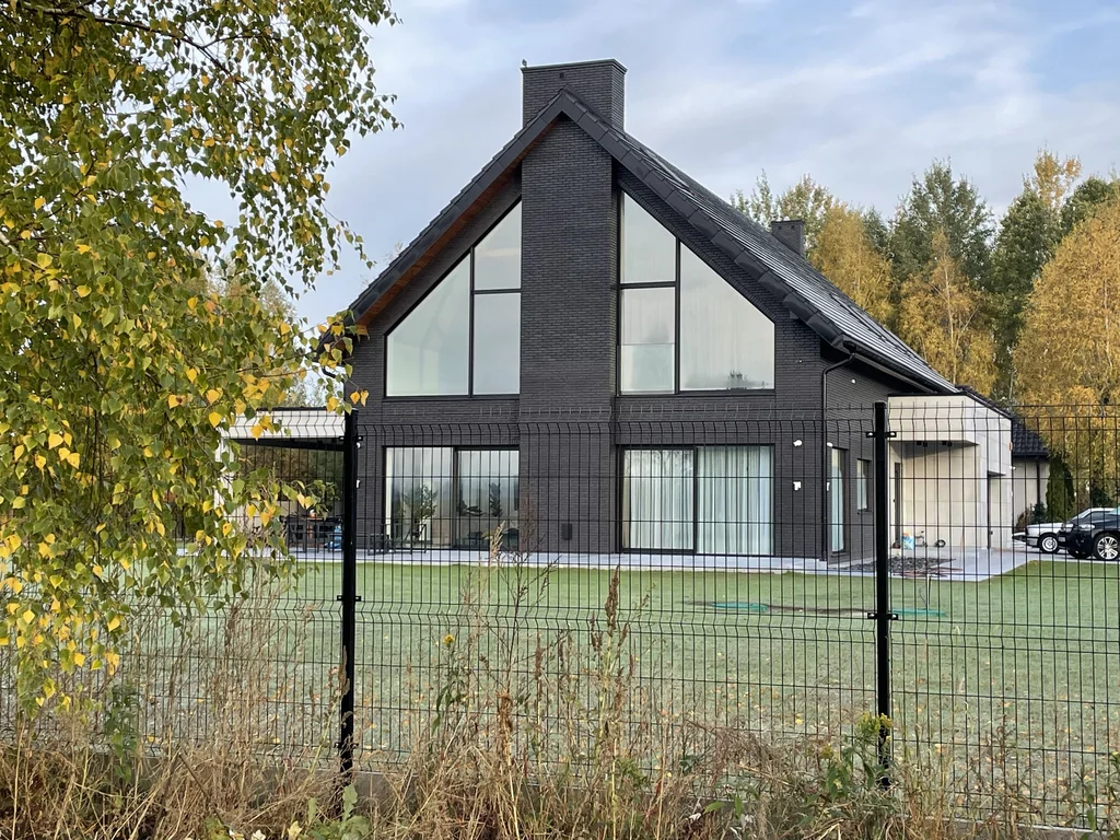 Elewacja szczytowa z wysokimi przeszkleniami – dom w Ruścu, widok przez ogrodzenie