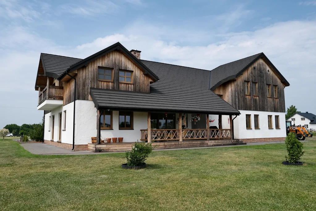 Boczny widok domu z drewnianą elewacją i balkonem oraz zadaszoną werandą na słupach