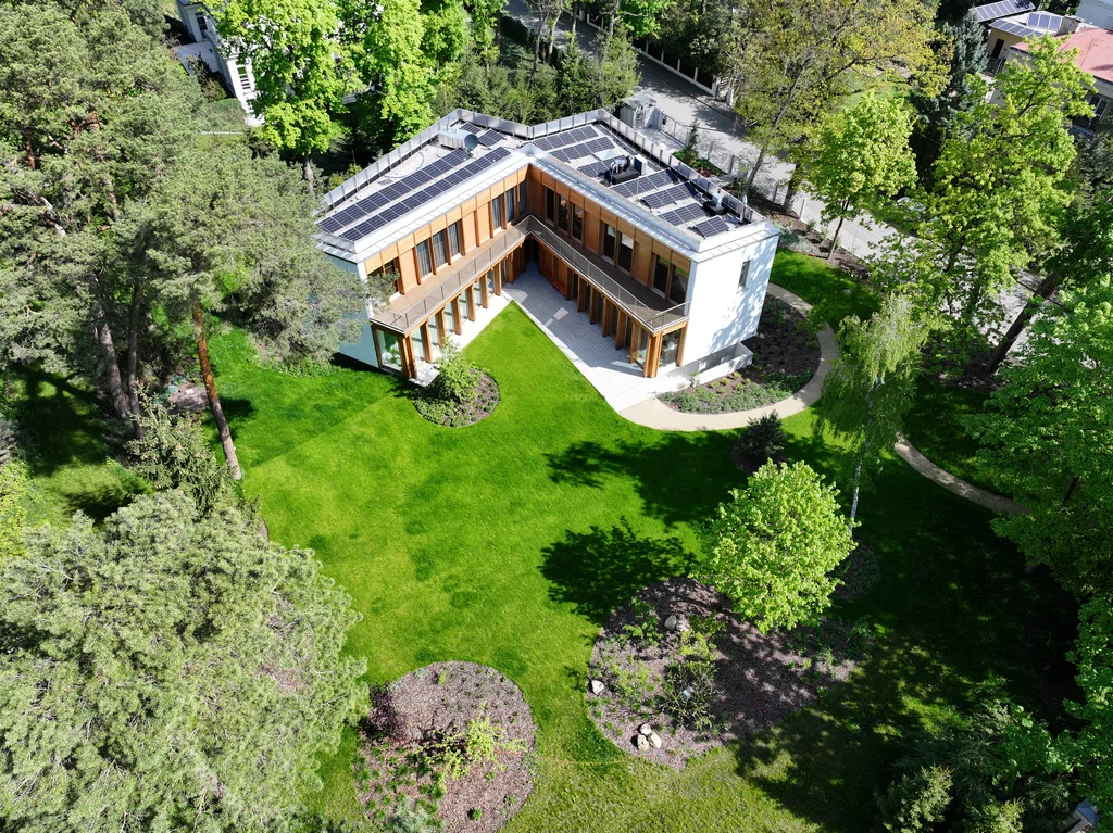 Ujęcie z lotu ptaka na nowoczesny dom z dużym ogrodem, rozległym trawnikiem, panelami fotowoltaicznymi na dachu i otaczającymi go drzewami