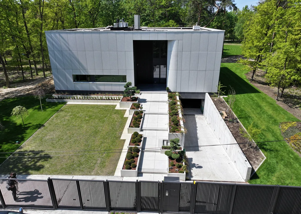 Widok z drona na front posesji z nowoczesnym domem, głównym dojściem oraz zjazdem do garażu podziemnego