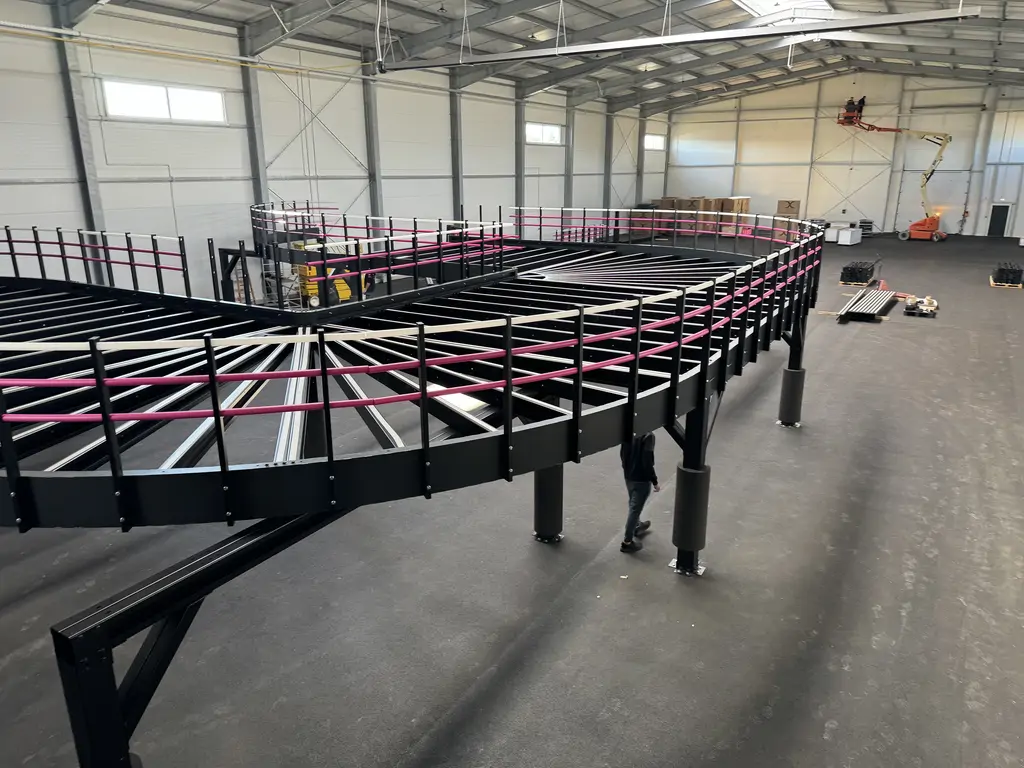 Ogólny widok wnętrza hali gokartowej na etapie wykończenia, z antresolą, rampą i materiałami do zabudowy.