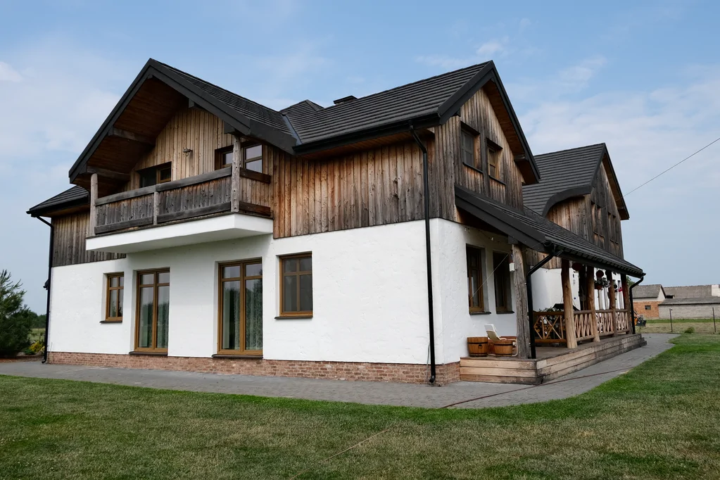 Boczny widok domu z drewnianą elewacją i balkonem oraz zadaszoną werandą na słupach