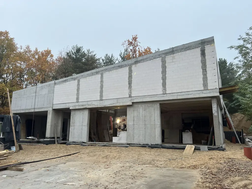 Frontowa elewacja domu w stanie surowym z dużymi otworami okiennymi i żelbetowym szkieletem.