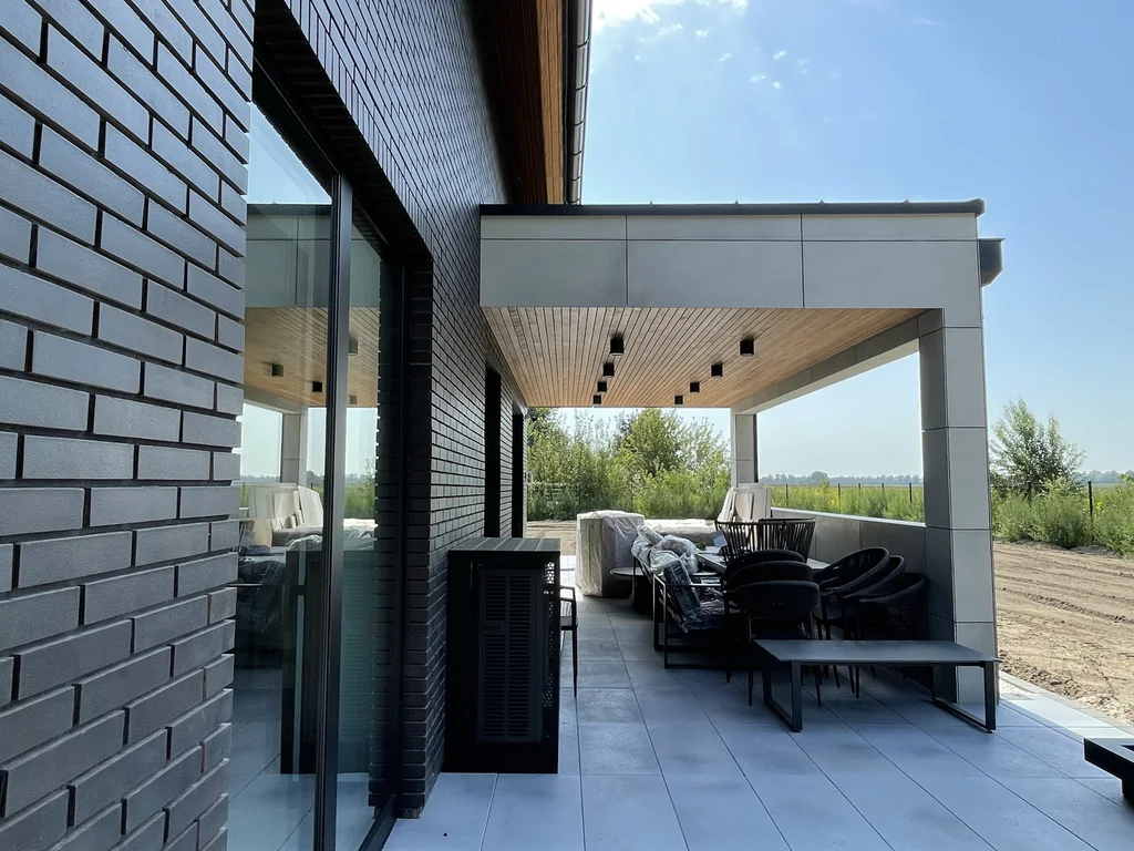 Taras pod zadaszeniem – widok wzdłuż elewacji z cegły, strefa wypoczynku