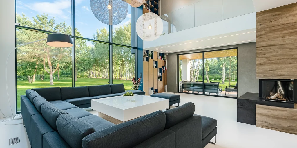 Salon z narożną sofą, wysokimi oknami i nowoczesnym kominkiem narożnym.