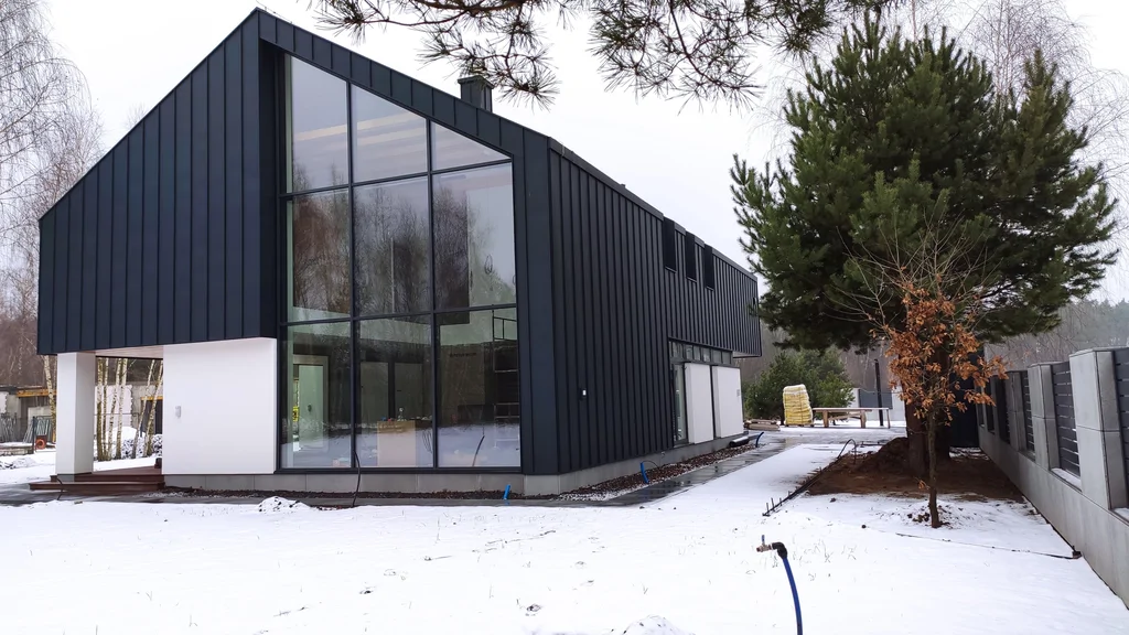 Nowoczesny dom zimą z wysokim przeszkleniem frontowym i czarną elewacją z blachy
