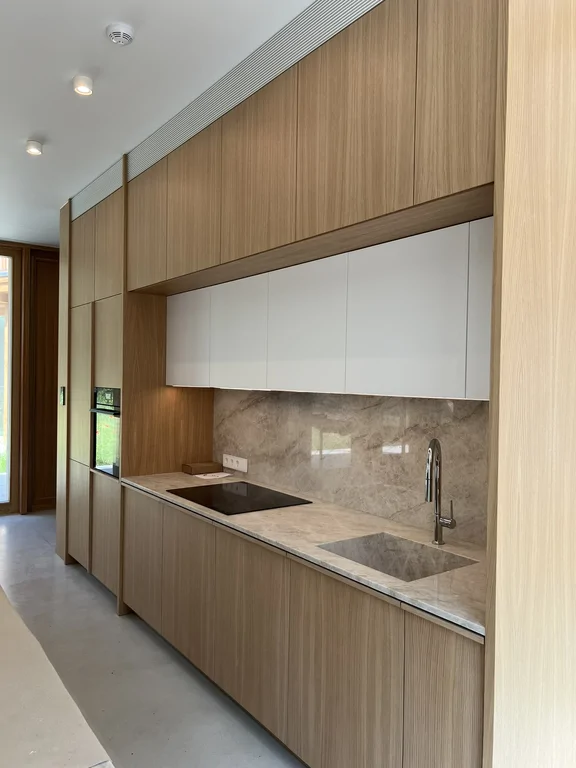 Zabudowa kuchenna z drewnianymi frontami, kamiennym blatem i białymi szafkami górnymi