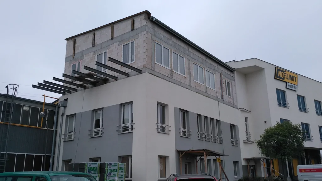 Widok na nadbudowany budynek z zewnątrz z wystawionymi belkami pod taras, ściany z silka 