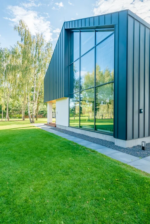 Boczne ujęcie elewacji szczytowej z pełnowysokościowym przeszkleniem i ciemną okładziną blaszana.