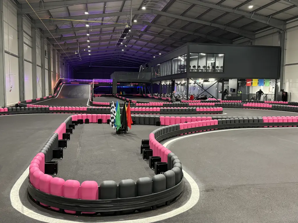 Widok z przeszklonej antresoli na tor gokartowy w trakcie wykończenia oraz zaplecze techniczne z materiałami budowlanymi.